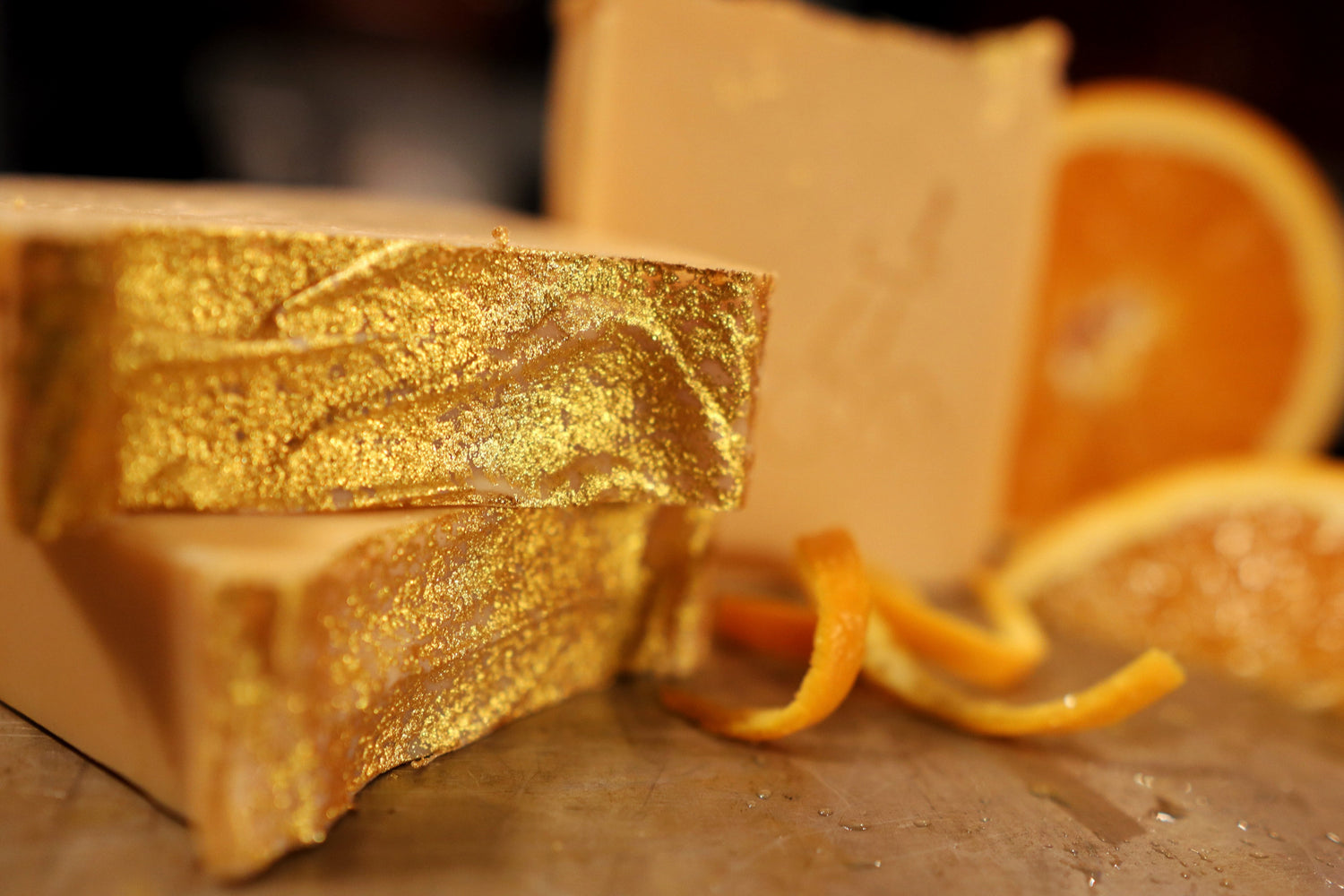 3 bars of orange soap dusted with gold and displayed with sliced oranges and zest slivers