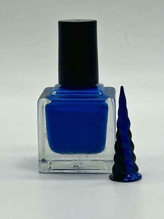 bright blue nail polish in a square glass bottle with black lid next to a small black unicorn horn that has the paint dripping down from it tip